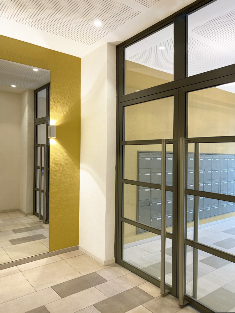 Hall d'entrée jaune et anthracite, avec un grand miroir, designé par Interface design pour un promoteur